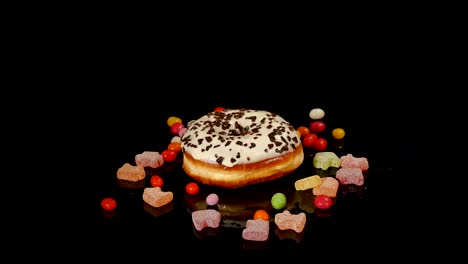 blanco gracioso sorprendido rosquilla esmaltada con salpicaduras, dulces de caramelo a rayas, dragee colorido con pasas o cacahuetes en el interior girar sobre fondo negro