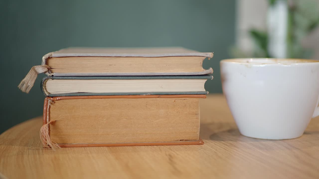 una pila de libros y una taza de café en una mesa de madera