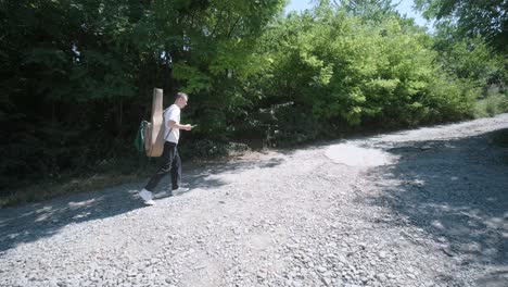 young man walking with guitar on street near forest