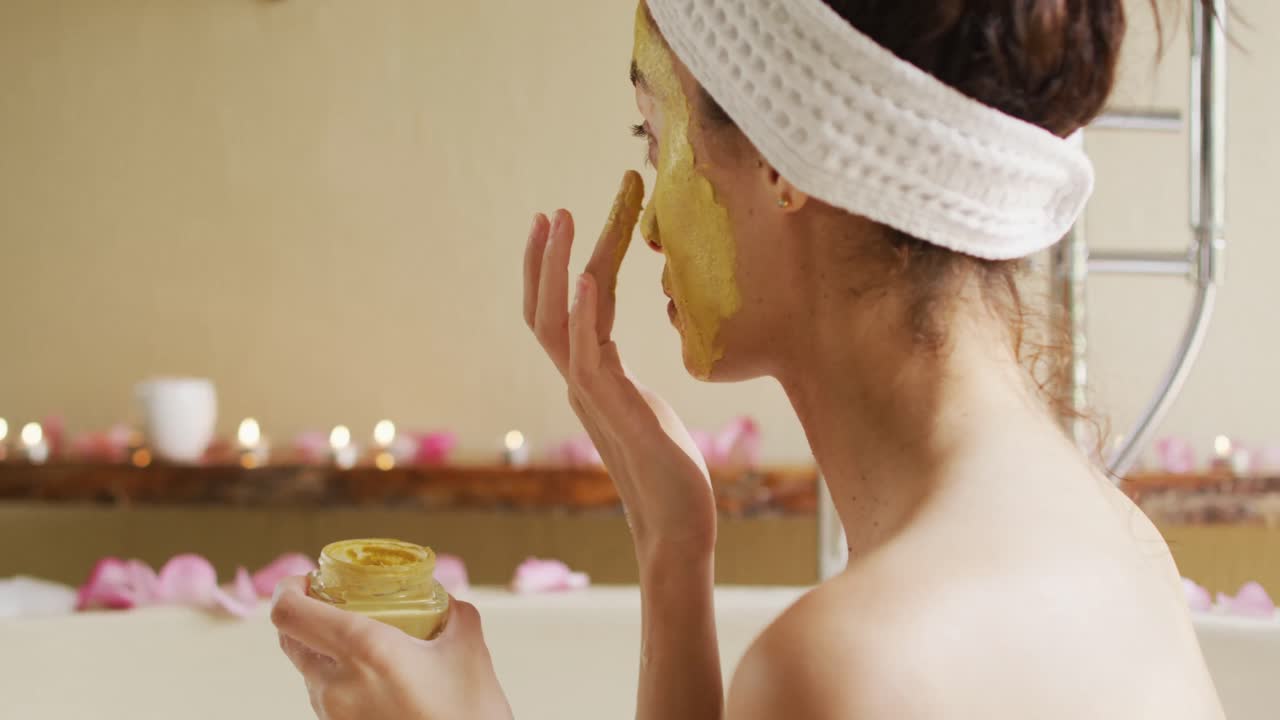 목욕실 에서 백내장 을  ⁇ 고 있는 두 인종 의 여성 이 거울 을 보고 얼굴 마스크 를 쓰고 있는 모습