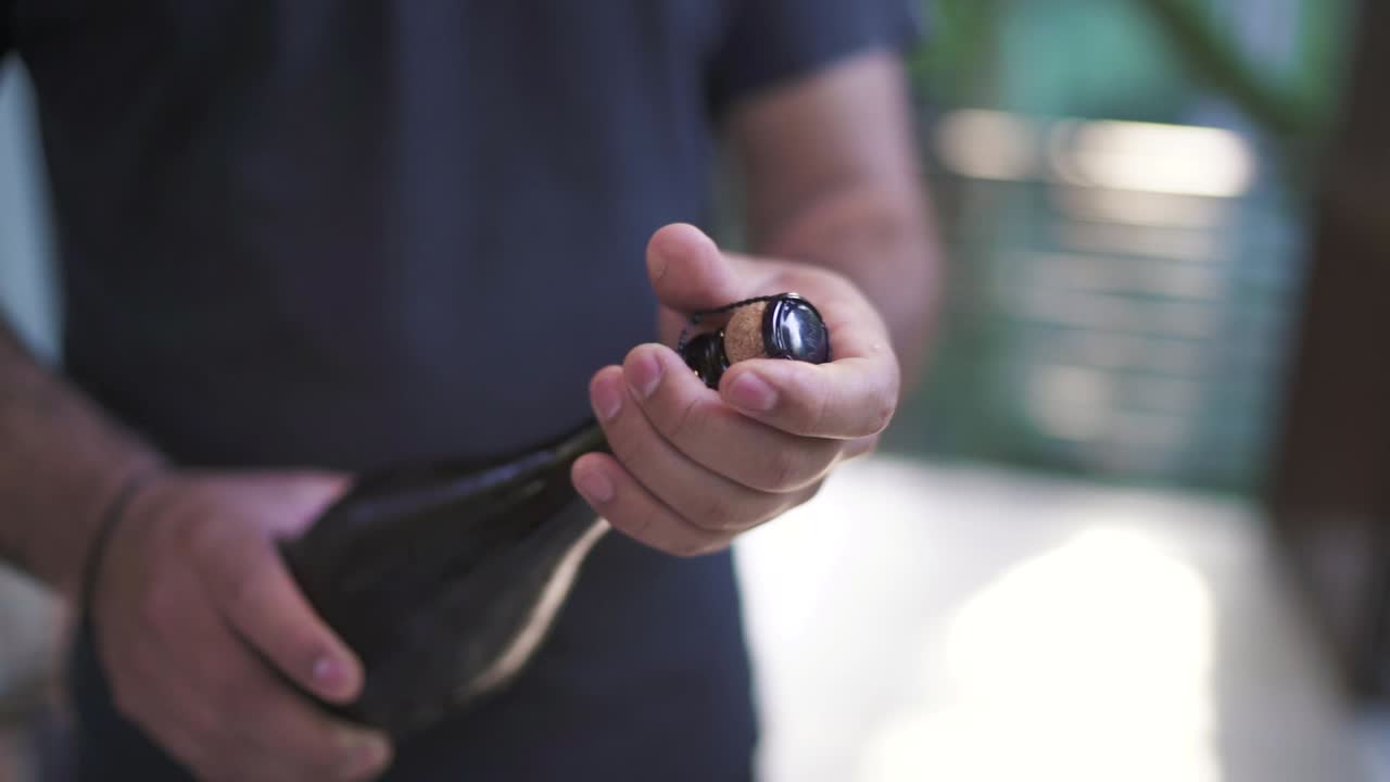 un primer plano en un restaurante con las manos del camarero, una botella de champán blanca abierta para la celebración.