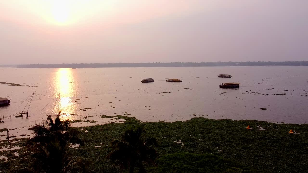Solnedgang over Keralas elvemunninger med husbåter og kinesiske fiskegarn i Alleppey, India