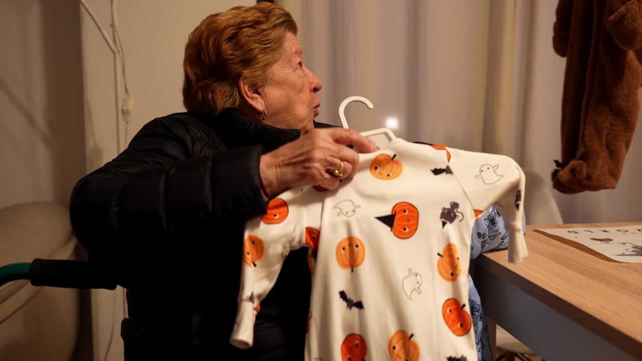Elderly woman holding baby onesie with Halloween pattern for future grandchild