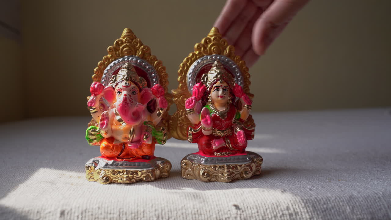 hands placing mini clay sculptures of Hindu lord Ganesha and Goddess laxmi on a table