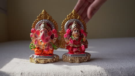 hands placing mini clay sculptures of hindu lord ganesha and goddess laxmi on a table