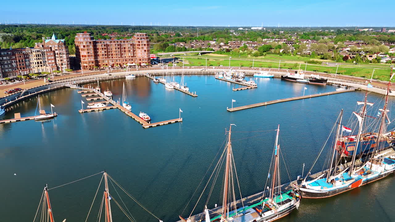 Marina of Lelystad, the Netherlands with few boats and ships at the berths. Cityscape with lush greenery at backdrop. Aerial view.