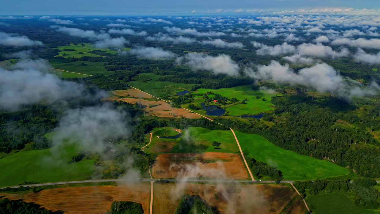 Green landscape of Latvia with low flowing clouds, aerial view