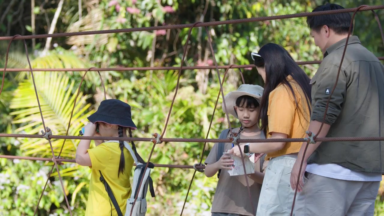 ครอบครัวกำลังสำรวจเส้นทางป่าเขียวชอุ่ม ข้ามสะพานแขวนเชือกในเวลากลางวันที่สดใส