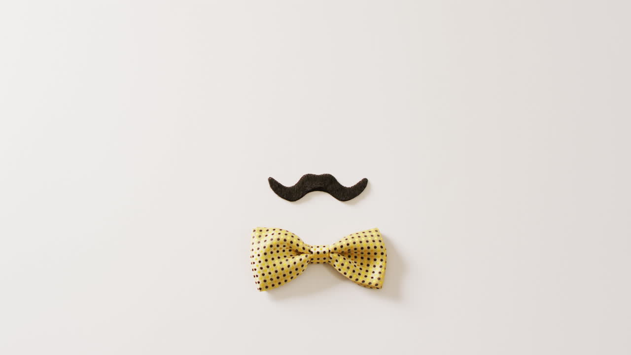 Video of black false moustache and yellow spotted bow tie on white background with copy space