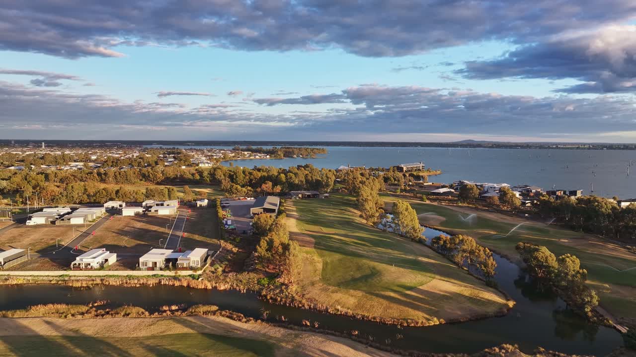 Houses and green fairways overlook Lake Mulwala with townscape and trees in soft sunset light
