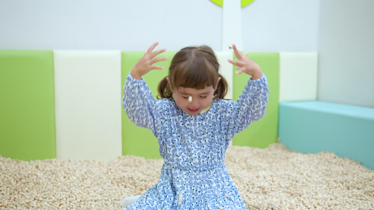Happy Smiling Child Girl Throws Hinoki Wood Cubes on Her Head Playing in Sand Pit Inside Playroom