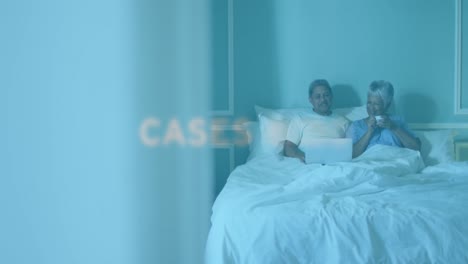 animation of covid 19 text over senior couple at home using laptop in bed