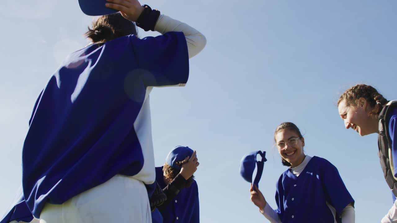 여성 야구 선수들의 행복한 다양한 팀이 공중에 모자를 던지고 경기 후 축하하고 있습니다.