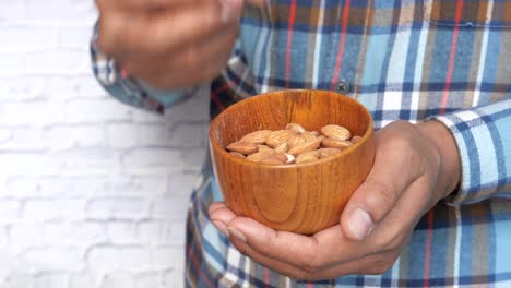 Person eating almonds from a wooden bowl