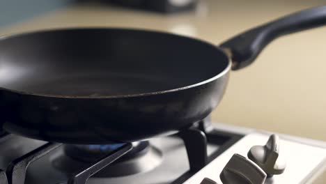 Close-up-slow-motion-shot-of-hands-placing-fry-pan-onto-gas-cook-top-stove-flame-food-preparation-in-kitchen-hospitality-health-food-4K