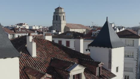 drone over historic maison louis xiv with turrets, rooftop, saint jean baptiste church tower in saint-jean-de-luz, sunny day, basque architecture, france. aerial forward