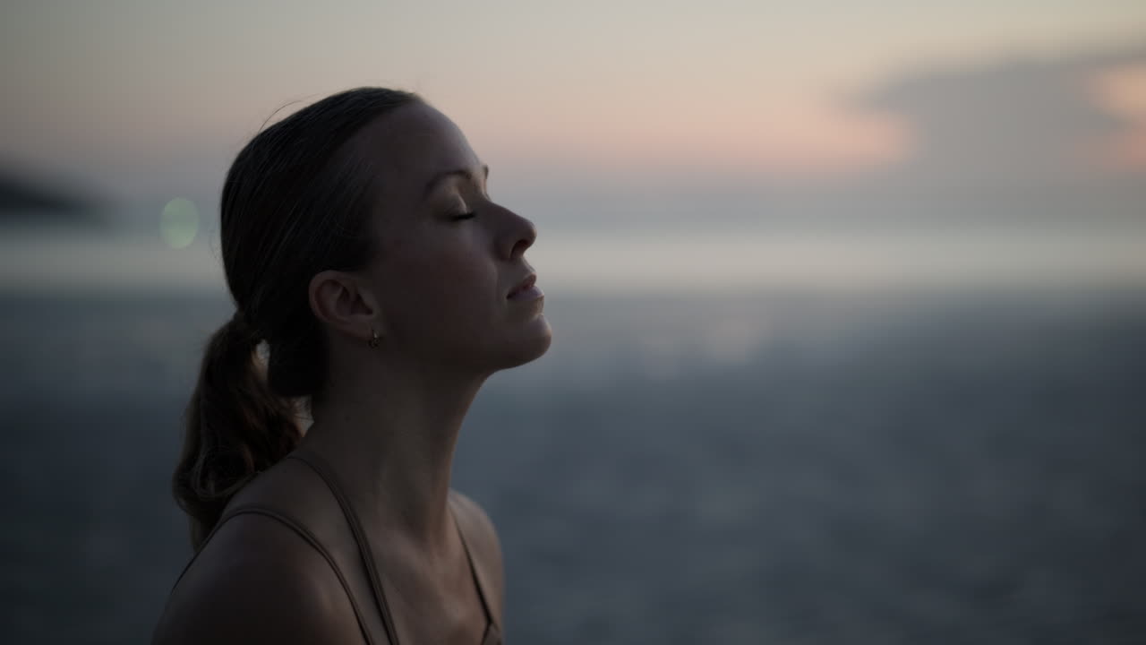 Donna serena con gli occhi chiusi in meditazione all'aperto al tramonto