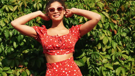 mujer en un vestido de impresión floral posando frente a una pared de vid verde