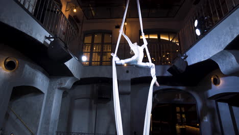 female aerialist doing a front split pose on silks with her knees bent