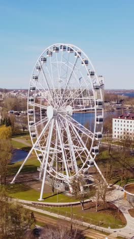 a vertical dolly shot pulling away from the ferris wheel, revealing the lush green park surroundings.