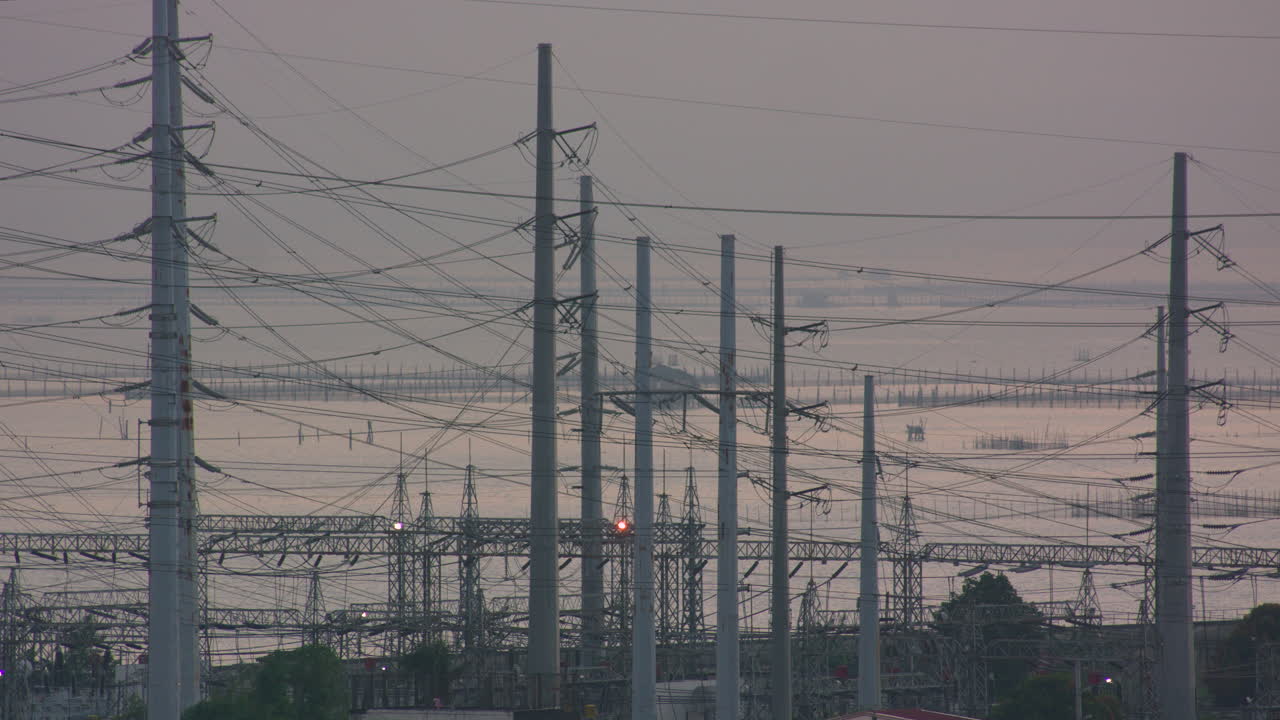 Static Shot Of Steel Posts And Power Lines With Body Of Water In The Background