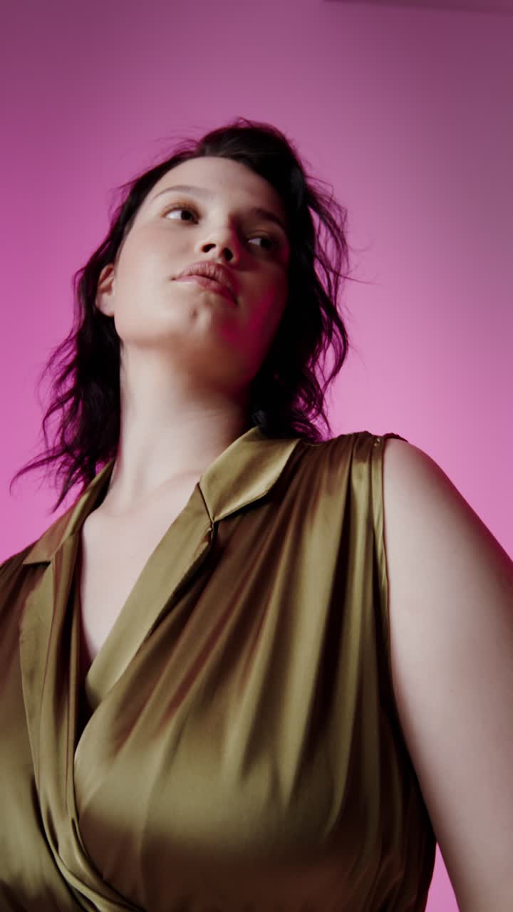 Elegant woman in olive green satin dress posing against a pink background