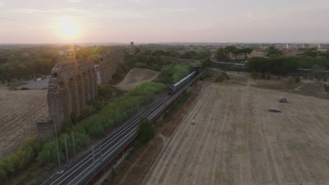 train passing by roman aqueduct ruins at sunset