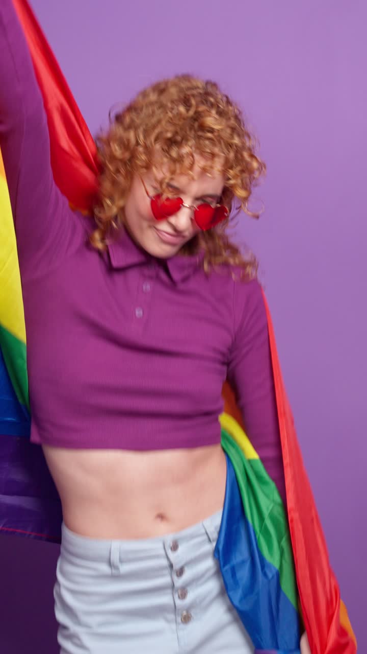 Woman with curly hair and heart sunglasses holding a pride flag