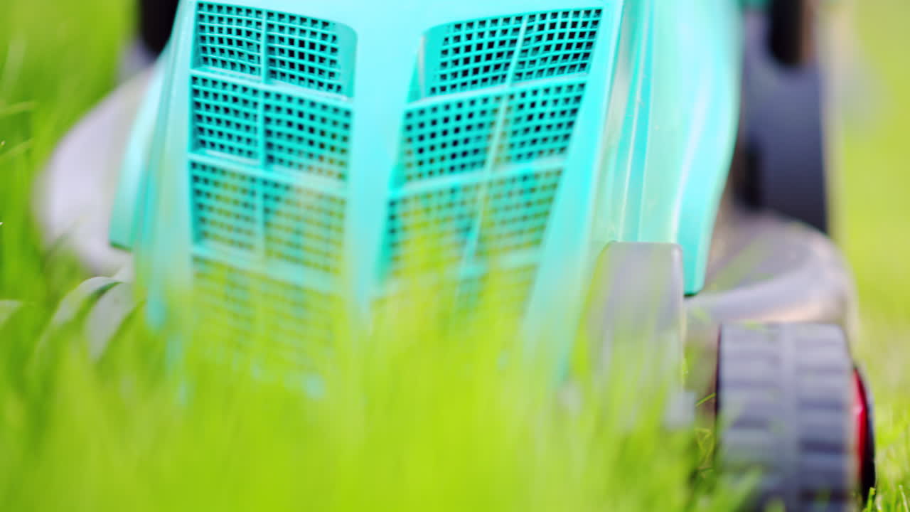 Close up of turquoise lawn mower machine cutting the grass