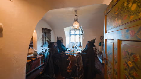 four figures of old witches wearing black clothes sitting at the table. decorated room with spider web in bran castle, romania.