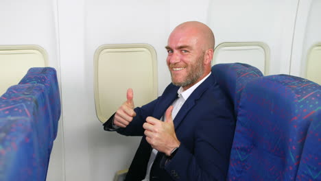 feliz hombre atractivo en un avión de pasajeros dando dos pulgares hacia arriba y sonriendo volando como un pasajero en vacaciones