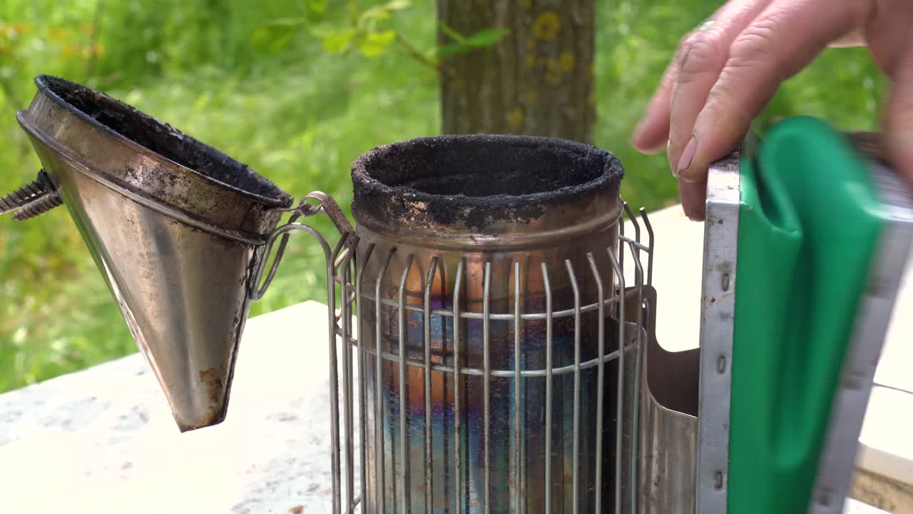 Beekeeper preparing a smoker tool outdoors for calming bees in the apiary