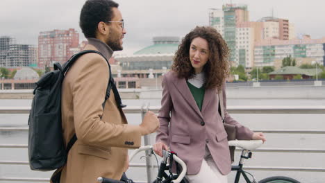 hombre y mujer americanos hablando entre ellos mientras se apoyan en sus bicicletas en el puente de la ciudad 1