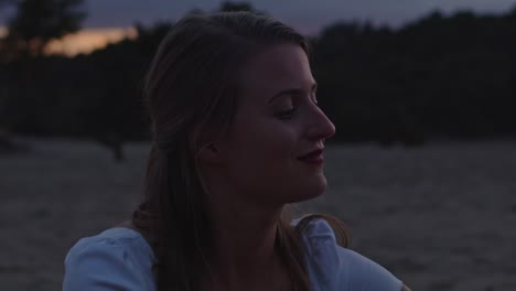 close up of attractive young woman sitting in sand dunes at dusk