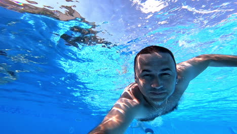 swimmer swims forward while looking at camera underwater. man swimming in clear water with underwater camera inside the swimming pool. summer vacation.