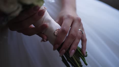 bride’s hands holding bouquet wrapped in ribbon with delicate brooch