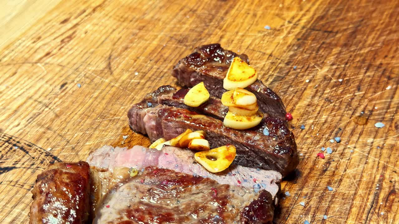 Bistecca a fette su tagliere di legno rustico con aglio arrosto e succhi versati sulla carne - Primo piano