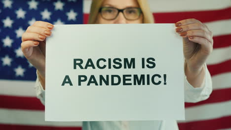 Junge-Frau-Hält-Ein-Plakat,-Das-Besagt,-Dass-Rassismus-Auf-Dem-Hintergrund-Der-Amerikanischen-Flagge-Eine-Pandemie-Ist