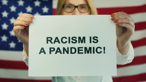 young woman holds poster stating racism is pandemic on american flag background