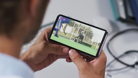 compuesto de un médico masculino viendo un partido de hockey en un teléfono inteligente