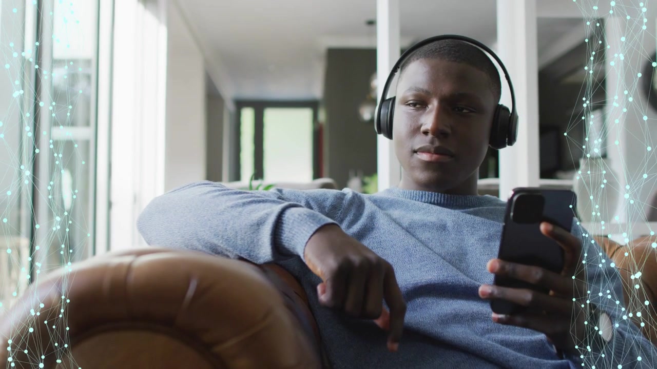 Un uomo tocca il telefono sul divano, mettendo in pausa e osservando per controllare la luce mentre particelle tecnologiche incorniciano il soggetto.