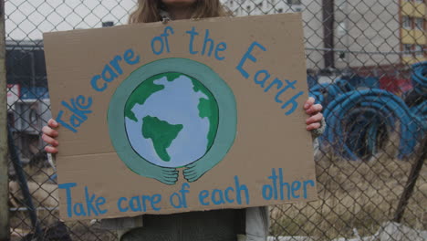 joven activista sosteniendo un cartel de cartón durante una protesta por el cambio climático mientras mira la cámara 1