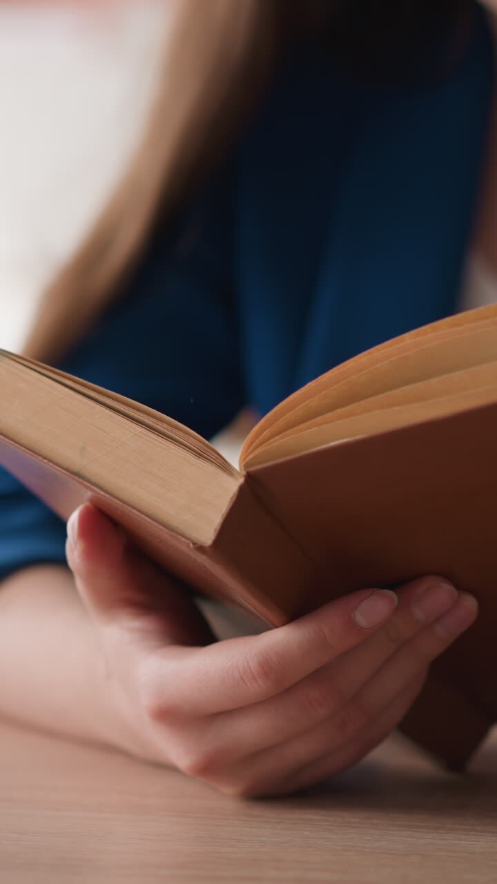 Woman turns pages of old book in library closeup. Lady in formal jacket reads vintage novel at desk in college. Visitor works with literature for essay