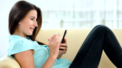 joven feliz usando su teléfono inteligente en el sofá en el interior