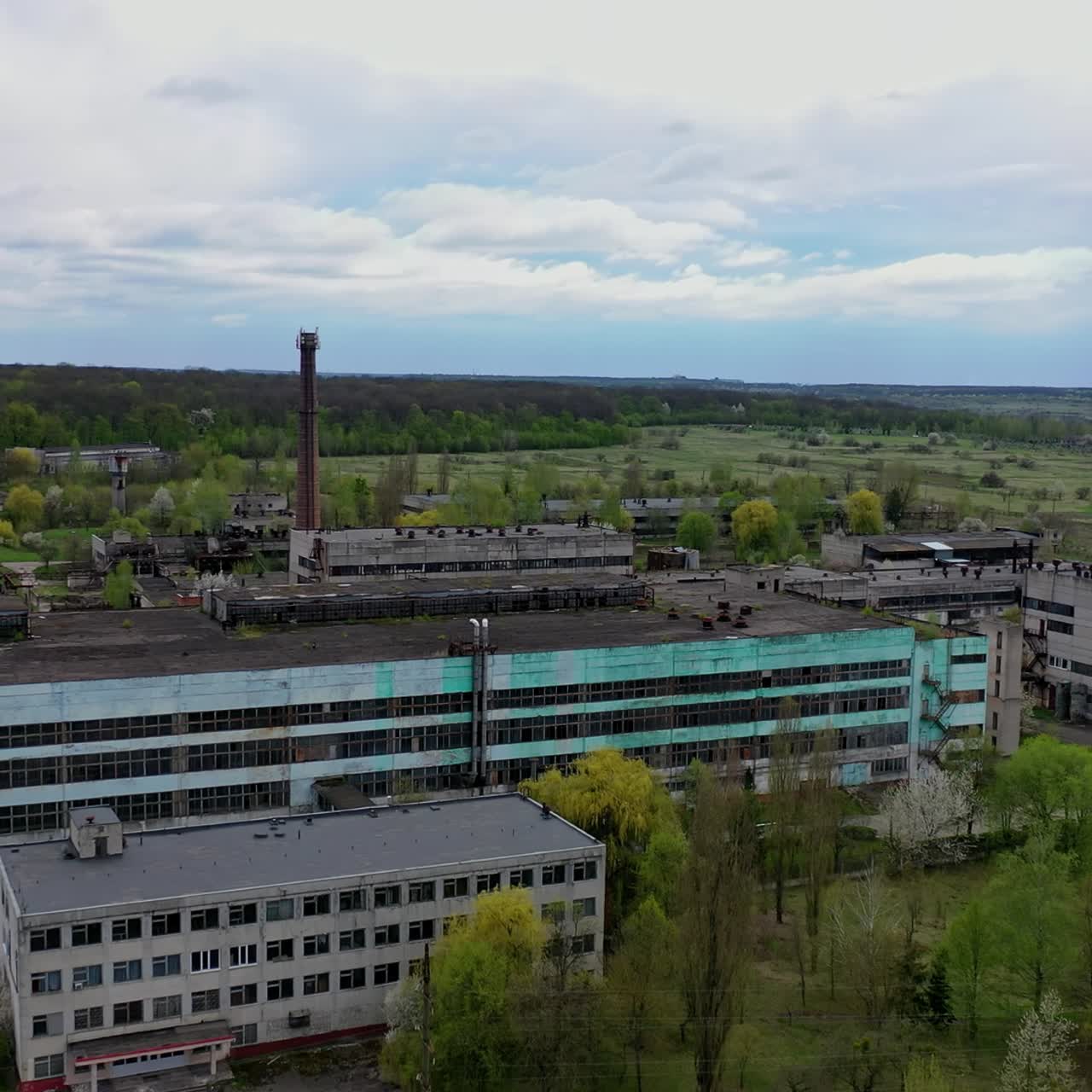 Large factory among beautiful green nature. Exterior of industrial plant in the countryside. Old architectural buildings of a manufacturing