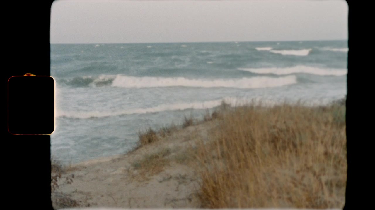 Ocean waves crashing on a sandy beach with dunes on Super 8 film