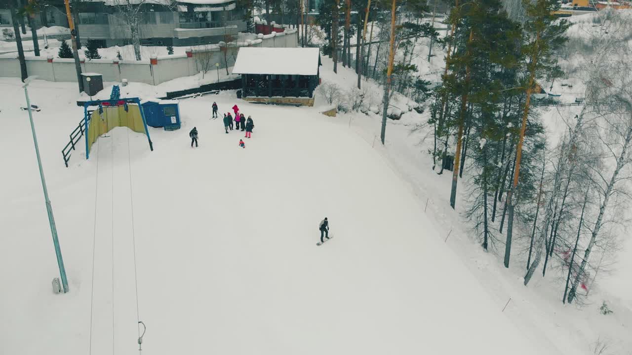한 무리의 사람들이 눈 덮인 슬로프를 내려가는 스노보더를 지켜봅니다.