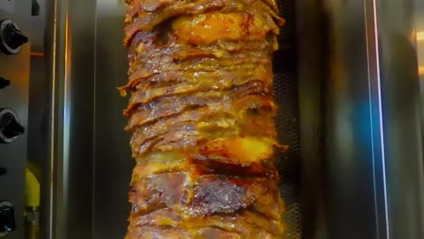 continuous loop 5 of 5 closeup of stacked marinated sirloin steaks thinly sliced onto a vertical stainless steel spit bbq with herbs and spices slowly cooking in rotation as juices drip down the meat