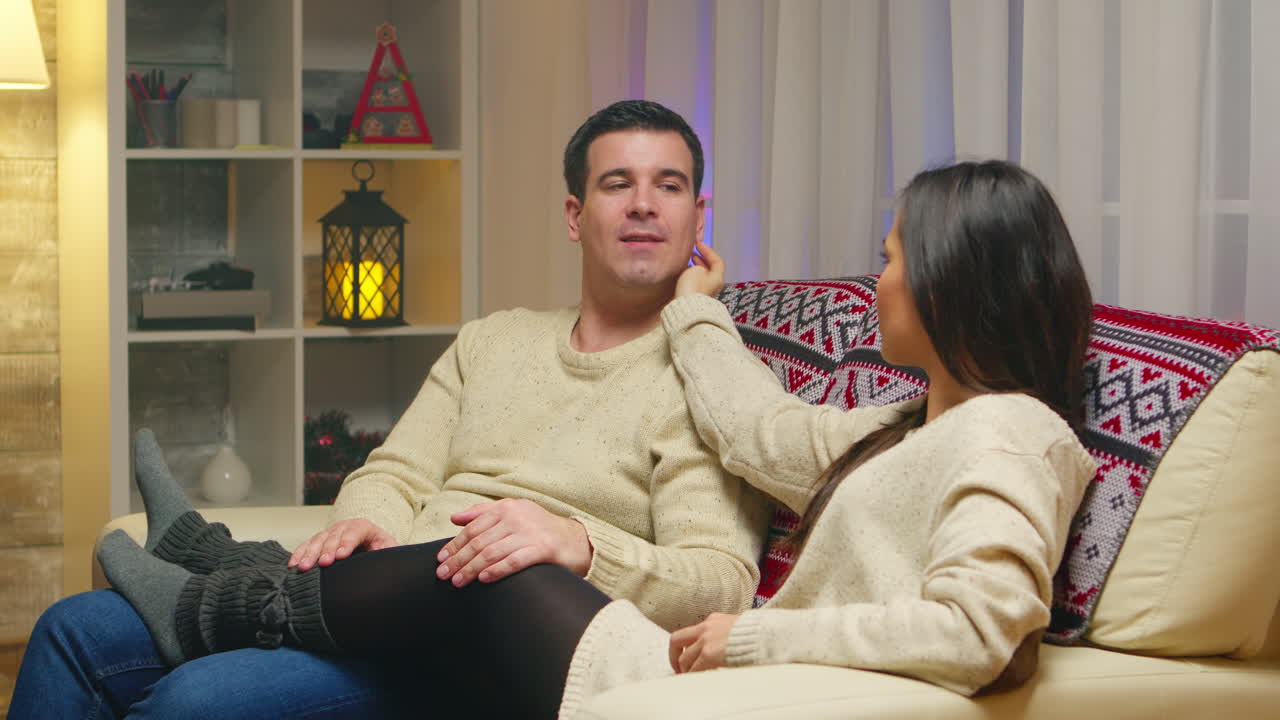 로맨틱한 젊은 부부가 소파에서 휴식을 취하고 크리스마스를 축하하고 있습니다.