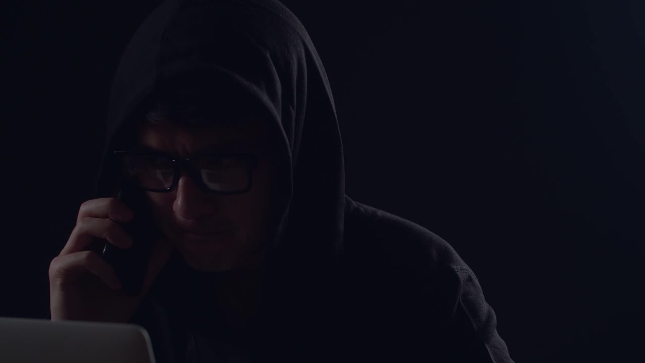 Asian Male Hacker Using Laptop Computer Hacking And Talking On Phone